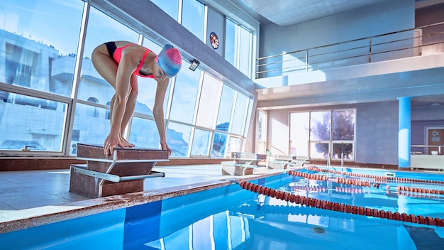 Nadadora campeona atlética deportiva en posición baja en el bloque de salida en una piscina