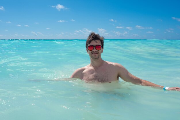 Nadando en el mar claro un joven con gafas de sol nadando en el mar Caribe