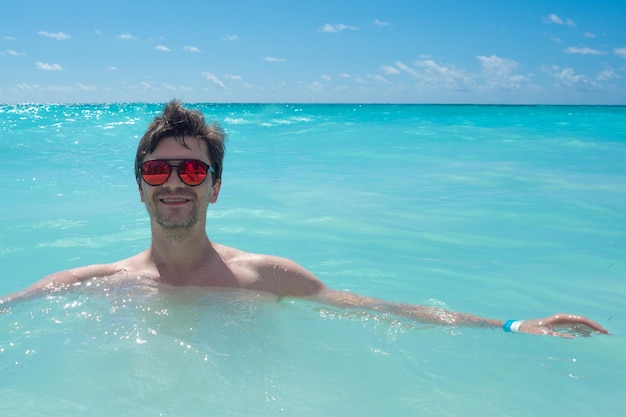 Nadando no mar claro, um jovem de óculos escuros nadando no mar do caribe, água azul, relaxi