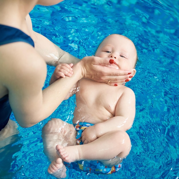 Foto nadar seguro com a ajuda da mãe na piscina vista superior do menino calmo criança focada na fralda nadando nas costas