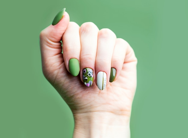 Nägel Design. Hände mit hellgrüner und weißer Maniküre auf Grün