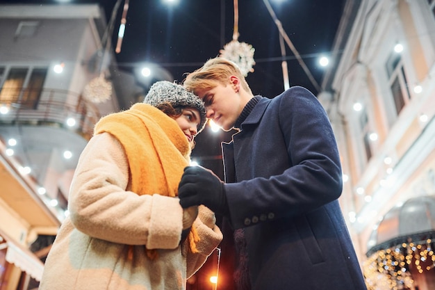 Nähe der Menschen. Glückliches junges Paar in warmer Kleidung ist zusammen auf weihnachtlich dekorierter Straße.