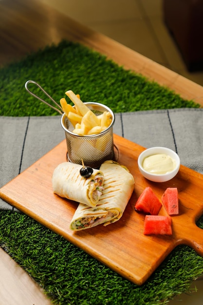 Naga-Beef-Ei-Wrap-Rolle gefüllt mit Tomaten-Zwiebel-Gurke mit Pommes-Mayonnaise und Wassermelonenscheiben-Dip, serviert auf einem Holzbrett, Draufsicht auf die Fastfood-Vorspeise