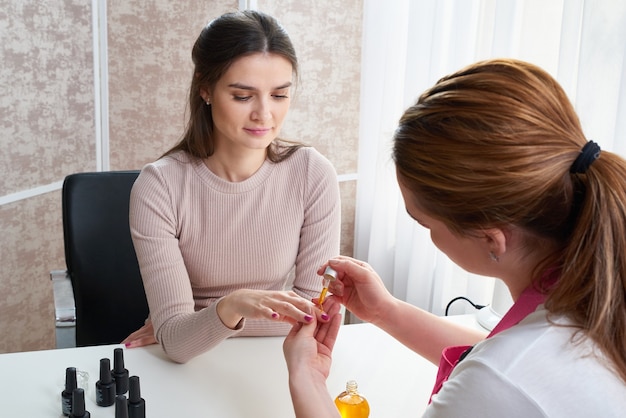 Nagelhautpflege. Weibliche Hand, die Öl auf Nägel aufträgt