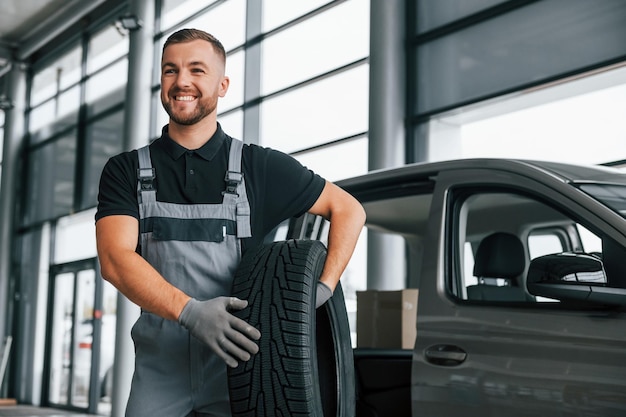 Nagelneuer Reifen Mann in Uniform arbeitet tagsüber im Autosalon