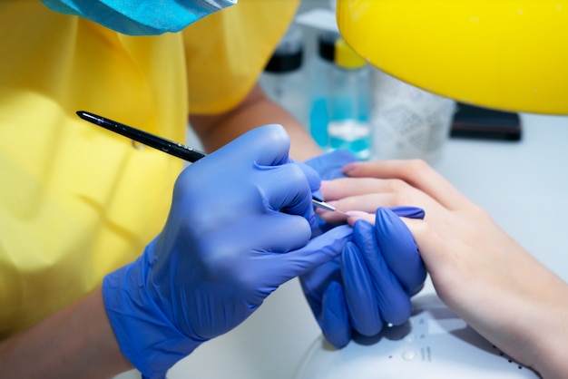 Nagelpflege. Maniküre im Salon. Der Meister manikürt das Mädchen, Schönheit und Gesundheit. Maniküre-Prozess. Meister in Maske und Handschuhen.