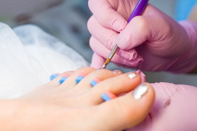 Nagelpflege- und Pedikürekonzept. Nahaufnahme-Maniküristhände in den rosa Handschuhen malt Goldnagellack auf den Zehen des Kunden.