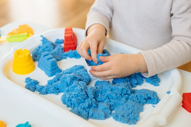 Nahansicht der Kinderhände, die mit kinetischem Sand spielen. Kreatives Spiel für Kinder für frühe Entwicklung und Feinmotorik.