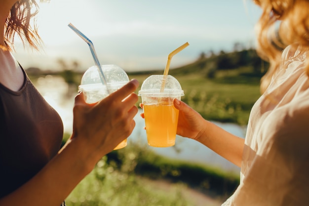 Nahansicht. Weibliche Haltebecher mit Cocktail. mit Stroh, bei Sonnenuntergang, positiver Gesichtsausdruck, im Freien