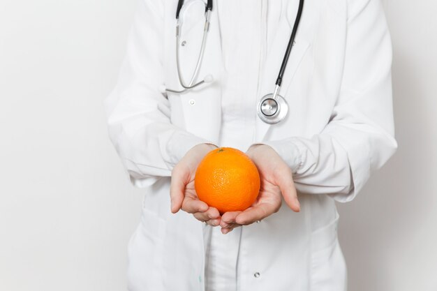 Nahaufnahme abgeschnittene junge Arztfrau mit Stethoskop isoliert auf weißem Hintergrund. Ärztin im medizinischen Kittel mit Orange. Gesundheitspersonal, Gesundheit, Medizinkonzept. Richtige Ernährung.