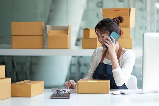 Nahaufnahme asiatisches Lächeln Frau erhält Bestellungen per Handy und hält die Hand in der Nähe des Laptops Kleinunternehmer KMU arbeiten mit Box zu Hause KMU-E-Commerce-Digitaltechnologie-Konzept