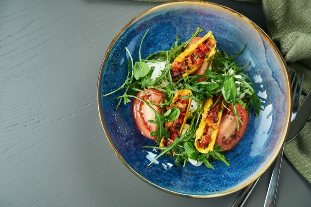 Nahaufnahme auf Appetitlich machenden italienischen Caprese-Salat mit frischen Tomaten, weichem Mozzarella, Rucola und Sauce in der blauen Schüssel rustikal. Draufsicht, Kopierraum, flache Lage