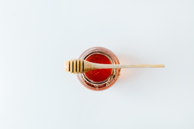 Nahaufnahme auf einem Glas Honig und einer Holzspindel für Honig auf weißem Hintergrund