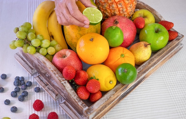 Nahaufnahme auf einem hölzernen Korb voller bunter, frischer Früchte Reife Frau die Hände halten eine halbe Limette Gesunde Ernährung und Lebensstil Weißer Hintergrund