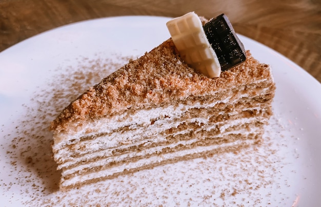 Nahaufnahme auf einem Tisch in einem Restaurant in einem weißen Teller ein Stück Honigkuchen mit weißer und Milchschokolade dekoriert.