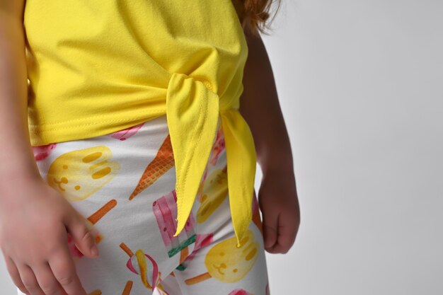 Nahaufnahme auf einer Krawatte auf einer gelben Baumwollbluse für Sommerkinder Ein kleines Kind demonstriert die Details der Kleidung