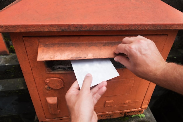 Nahaufnahme auf einer männlichen Hand, die einen Brief in einen roten Briefkasten legt Konzept der Vintage-Art der Kommunikation