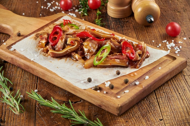 Nahaufnahme auf geräucherte Schweineohren in süß-saurer Sauce mit Chili auf Pergament auf einer Holzoberfläche in einer Komposition mit Gewürzen