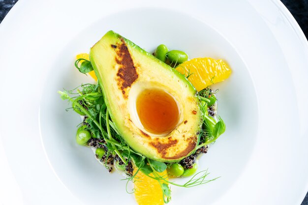 Nahaufnahme auf leckere gegrillte Avocado mit cremiger würziger Butter auf Pad mit Quinoa, Grün und Mikrogrün. Restaurant Essen Stil.