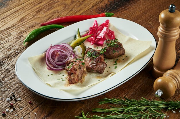 Nahaufnahme auf leckeres gegrilltes Fleisch mit Gemüse auf georgischer Pita. Schaschlik oder Grillfleisch auf Pita. Schaschlik, traditionelles Essen der georgischen Küche. Kopieren Sie Platz für Design. Holzoberfläche