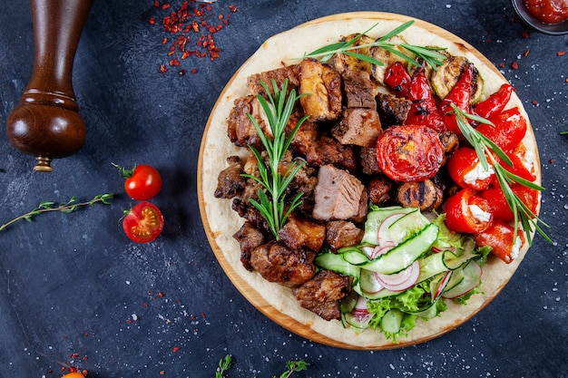 Nahaufnahme auf leckeres gegrilltes Fleisch mit Gemüse auf georgischer Pita. Schaschlik oder Grillfleisch auf Pita. Schaschlik, traditionelles Essen der georgischen Küche. Speicherplatz kopieren. Draufsicht. Dunkler Hintergrund