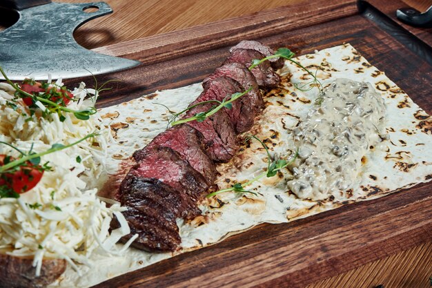 Nahaufnahme auf Rinderfilet oder geschnittenem Steak Medium selten mit einer Beilage aus Ofenkartoffeln und Pilzsalat auf einem Holzbrett. Biersnack, leckeres Essen