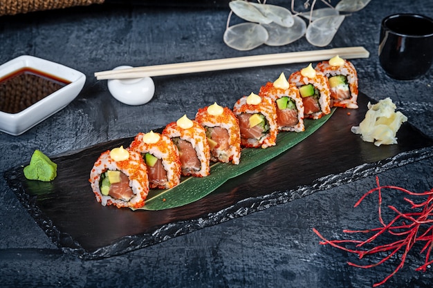 Nahaufnahme auf Satz Sushi-Rolle. California Roll mit Lachs, Avocado und Kaviar serviert auf schwarzem Stein auf dunklem Hintergrund. Japanische Küche. Speicherplatz kopieren. Serviert Sushi für Menü. Gesundes Essen, Meeresfrüchte