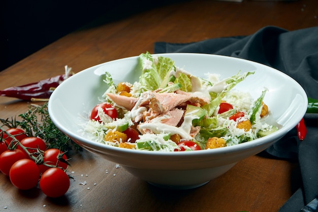 Nahaufnahme auf serviertem Caesar-Salat mit geräuchertem Lachs in weißer Platte auf Holztisch. Leckerer Meeresfrüchtesalat