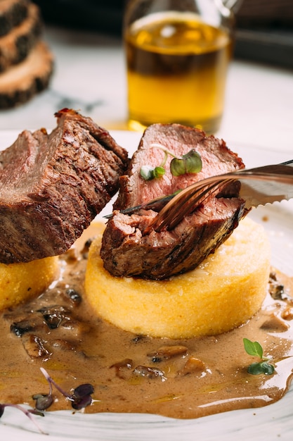 Nahaufnahme beim Essen von gebratenem Rindfleischmedaillon auf Maisbrei mit Pilzsauce