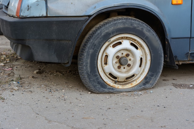 Nahaufnahme beschädigter Reifen. Das Rad des Autoreifens undicht. Reifenpanne wartet auf Reparatur. Verlassenes Auto auf dem Parkplatz.