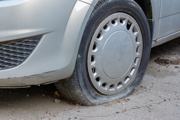 Nahaufnahme beschädigter Reifen. Das Rad des Autoreifens undicht. Reifenpanne wartet auf Reparatur. Verlassenes Auto auf dem Parkplatz.