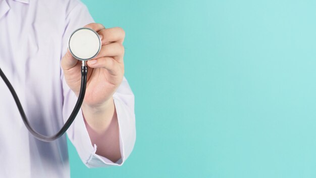 Nahaufnahme der Arzthand, die Stethoskop hält und ein langärmliges Kleid auf mintgrünem oder tiffanyblauem Hintergrund trägt