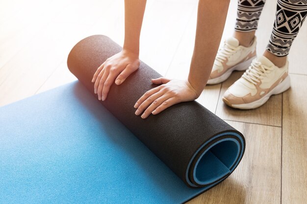 Nahaufnahme der attraktiven jungen Frau, die blaues Yoga oder Fitnessmatte faltet