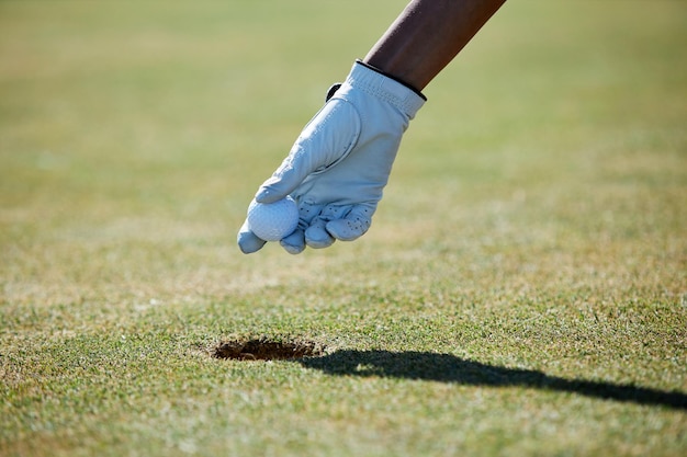 Nahaufnahme der behandschuhten Hand, die den Golfball aus dem Loch aufhebt