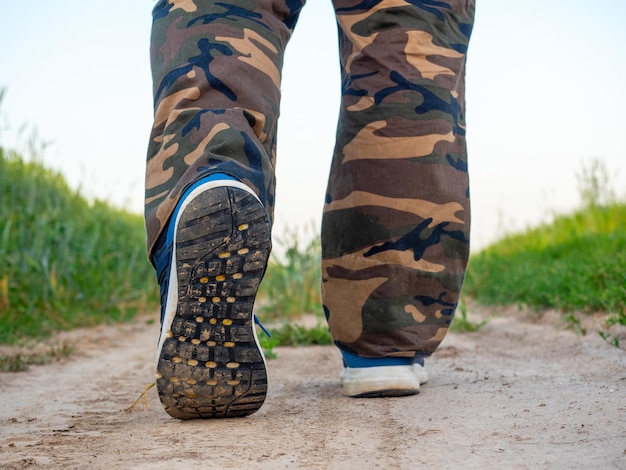 Nahaufnahme der Beine eines Mannes in Turnschuhen, der auf einem Weg im Wald spazieren geht Das Konzept des Wanderns und eine sportliche Lifestyle-Rückansicht