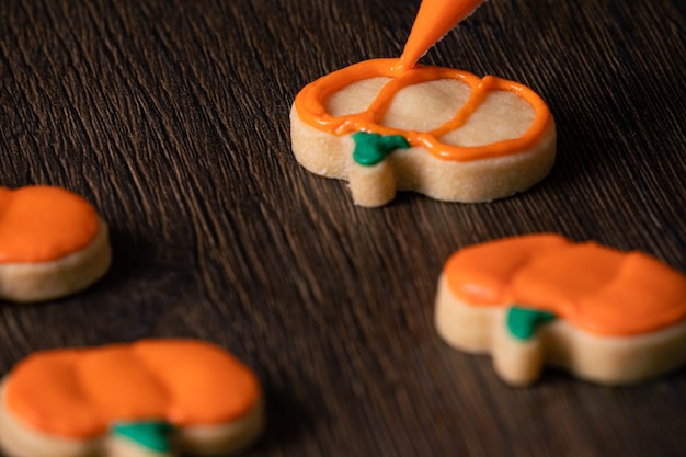 Nahaufnahme der Dekoration von süßen Halloween-Kürbis-Lebkuchenplätzchen mit Zuckerguss-Eiscreme-Topping-Tasche.