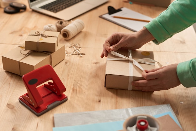 Nahaufnahme der Frau, die Geschenkbox mit Band am Tisch verziert