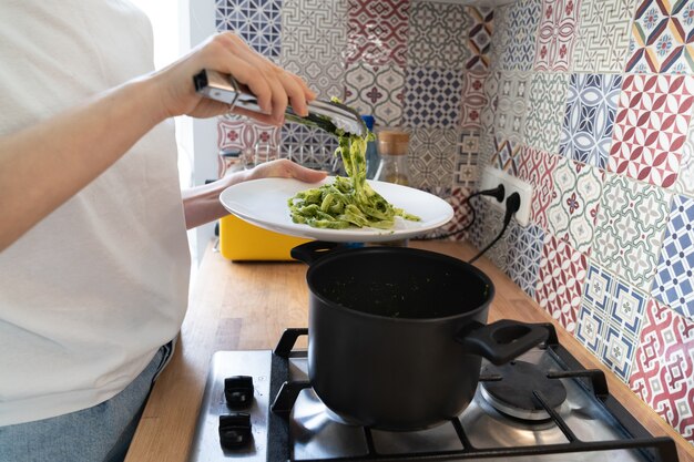 Nahaufnahme der frau legt die fettuccine-pesto-paste vom topf auf einen teller. hausgemachte italienische küche, echtes häusliches leben.