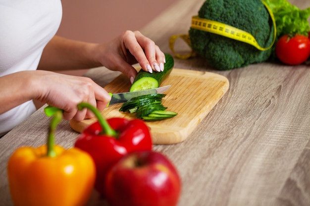 Nahaufnahme der Frau schneidet Gurke für frischen Salat