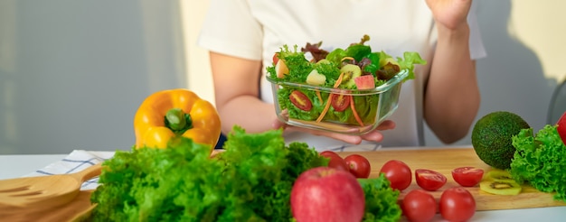 Nahaufnahme der Frauenhände, die Salatschüssel und verschiedene grünes Blattgemüse auf dem Tisch am Haus zeigen.