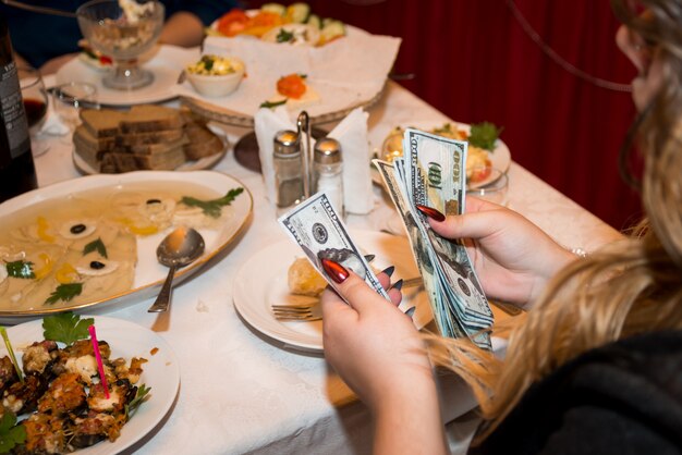 Nahaufnahme der frauenhände mit einer hellen maniküre, die geld-us-dollar zählt, in einem restaurant