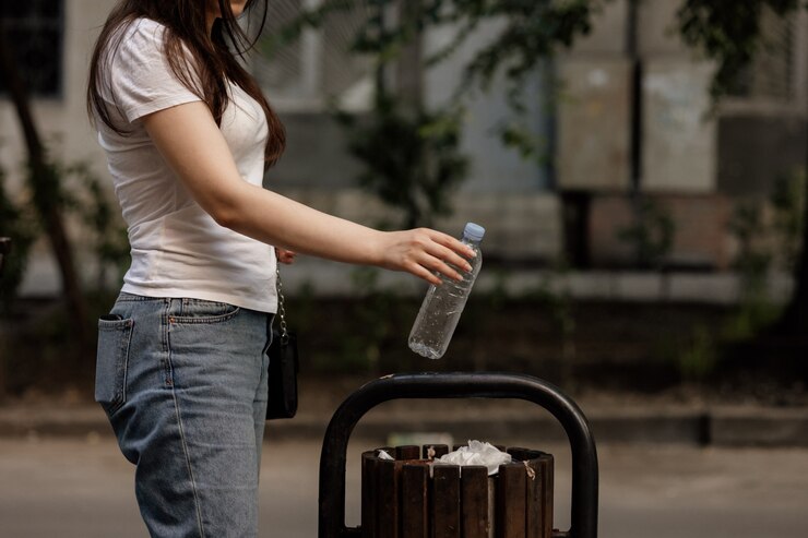 Nahaufnahme der Frauenhand, die leere Plastikwasserflasche im hölzernen Abfall wirft. Recycling-Konzept.