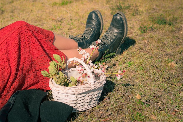 Nahaufnahme der Füße einer Frau auf dem Gras mit einem weißen Korb mit Mandelbaumblumen