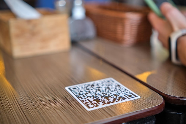 Nahaufnahme der Gästehand, die im Restaurant eine Mahlzeit bestellt, während sie den QR-Code mit dem Mobiltelefon für das Online-Menü scannt.