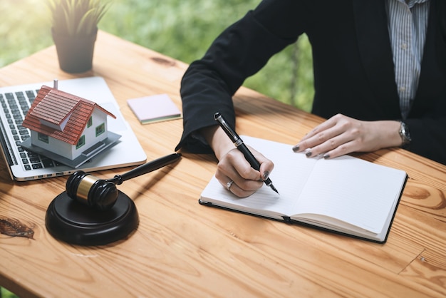 Nahaufnahme der Geschäftsfrau und des Anwalts Hand, die Stift hält und Notizen Mallet Laptop Musterhaus am Schreibtisch macht.