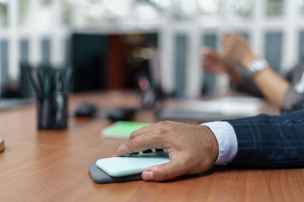 Nahaufnahme der Geschäftsmannhand, die während des Meetings ein Smartphone auf dem Tisch hält