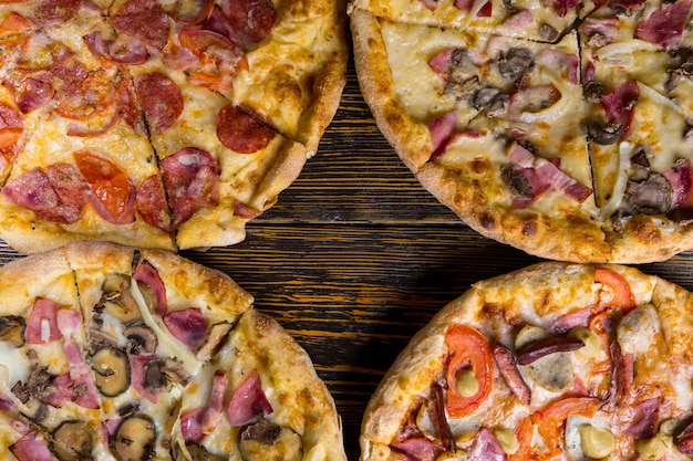 Foto nahaufnahme der hälfte von vier verschiedenen leckeren pizzen auf holztisch