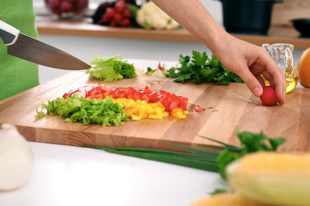 Nahaufnahme der Hände der Frau, die in der Küche kochen. Hausfrau, die frischen Salat schneidet. Vegetarisches und gesundes Kochkonzept.