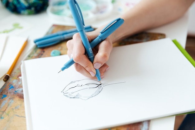 Nahaufnahme der Hände der Künstlerin, die mit Gel-Tintenstift auf dem Tisch zeichnet