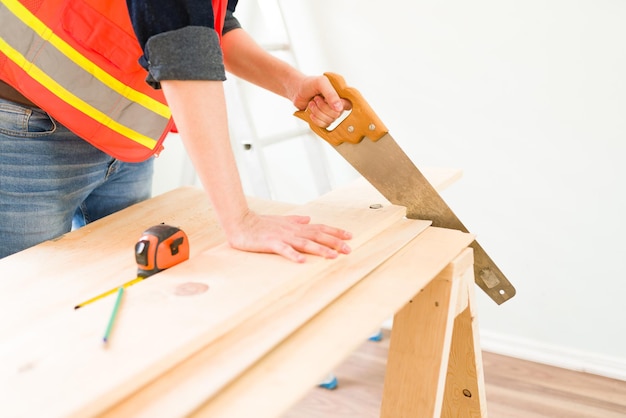 Nahaufnahme der Hände des Auftragnehmers, die Holz mit einer Säge schneiden. Männlicher Zimmermann, der mit Holz arbeitet, um eine neue Wand zu bauen